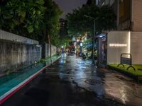 a wet street at night with street lights on and an empty bench at the end