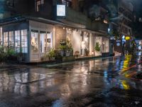 a wet sidewalk in the city at night near a cafe in the rain with lights shining