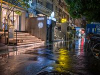 a rainy night with people walking on the sidewalk and parked vehicles on the street,