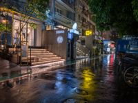 a rainy night with people walking on the sidewalk and parked vehicles on the street,