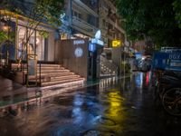 a rainy night with people walking on the sidewalk and parked vehicles on the street,