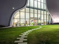 a building has a large circular window at night time in front of it, with a lawn outside of the building