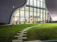 a building has a large circular window at night time in front of it, with a lawn outside of the building