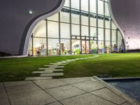 a building has a large circular window at night time in front of it, with a lawn outside of the building