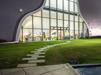 a building has a large circular window at night time in front of it, with a lawn outside of the building