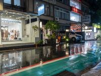 a wet sidewalk with a bunch of different storefronts on it at night,