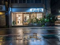 a store in the rain on the side of the street by the building with a blue sign saying, ohcher store