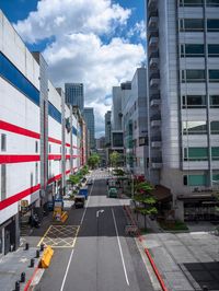 a narrow street surrounded by tall buildings with lots of parked cars on it, with a few windows and a light blue sky with wispeaking clouds