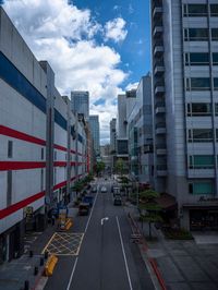 a narrow street surrounded by tall buildings with lots of parked cars on it, with a few windows and a light blue sky with wispeaking clouds