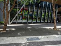 an empty street is lined with tall buildings and trees in front of the building is covered in mirrors