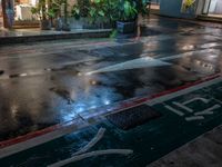 wet sidewalk with rain and red curb on it in front of restaurant at night with light coming down from windows