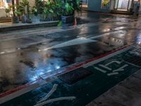 wet sidewalk with rain and red curb on it in front of restaurant at night with light coming down from windows