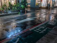 wet sidewalk with rain and red curb on it in front of restaurant at night with light coming down from windows