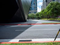 a yellow traffic light on top of a street next to tall buildings, near some grass, and red curb