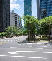 a road with a bus stop sign and green trees near tall buildings in the distance