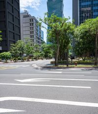 a road with a bus stop sign and green trees near tall buildings in the distance