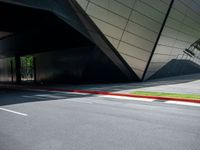 a road is in front of a modern building with an upward curved facade and red painted strip