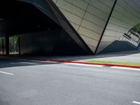 a road is in front of a modern building with an upward curved facade and red painted strip