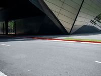 a road is in front of a modern building with an upward curved facade and red painted strip