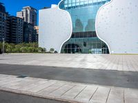 a building made of large white shaped glass and metal on a street near buildings under blue skies