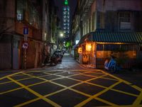 an alley with an umbrella, parked motorcycles and the oriental architecture at night - - a woman sits alone in the dark