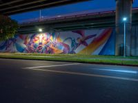 a wall painted with graffiti next to a road with a car driving past it at night