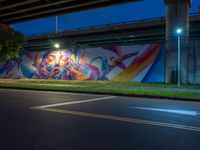 a wall painted with graffiti next to a road with a car driving past it at night