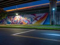 a wall painted with graffiti next to a road with a car driving past it at night