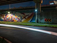 the bright streaks of light shine under a bridge painting in the dark, with the street under the bridge turning on