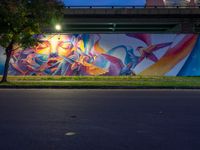 a mural on the side of a street near a bridge with lights coming down on the roof