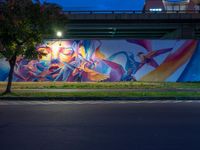 a mural on the side of a street near a bridge with lights coming down on the roof