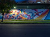 a mural on the side of a street near a bridge with lights coming down on the roof