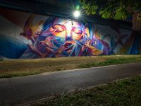 a person walking near a graffiti on the side of a road by grass and trees