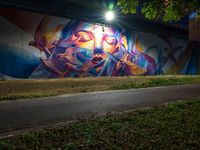 a person walking near a graffiti on the side of a road by grass and trees