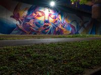 a person walking near a graffiti on the side of a road by grass and trees