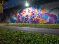 a streetlight shines down on a colorful wall painted by the graffiti artist who has painted his image