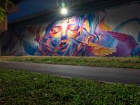 a streetlight shines down on a colorful wall painted by the graffiti artist who has painted his image