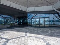 the ground is hexagonal tile with glass doors and windows reflecting a body of water