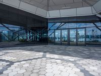 the ground is hexagonal tile with glass doors and windows reflecting a body of water