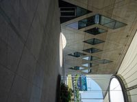 an elevated walkway with a glass ceiling next to trees and buildings next to it are many people and there is a skylight above