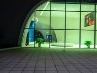 a very large glass and metal building with some plants outside it's windows at night