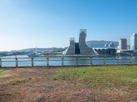 view of a city and water from the other side of a fence with grass growing in it