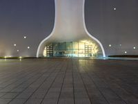 an empty building with a concrete floor in front of it at night time with lights shining on the side