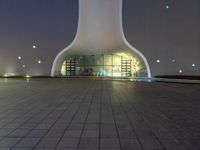 an empty building with a concrete floor in front of it at night time with lights shining on the side