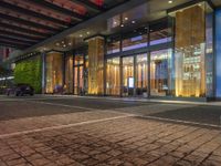 a building with large glass doors and illuminated windows in front of it at night time