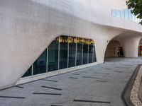 a paved walkway near a building that has a circular window with large glass panels at the entrance