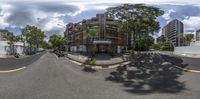 a photo of a building, trees, and a paved street with one motorcycle parked on the curb