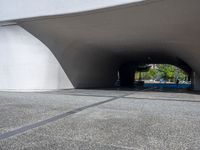 a person riding a skateboard through a tunnel under a large building overhanges