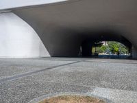 a person riding a skateboard through a tunnel under a large building overhanges