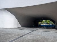 a person riding a skateboard through a tunnel under a large building overhanges